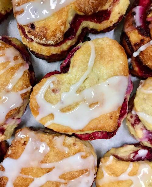 Heart-shaped pastries filled with fruit and drizzled with icing, arranged closely together on a tray.