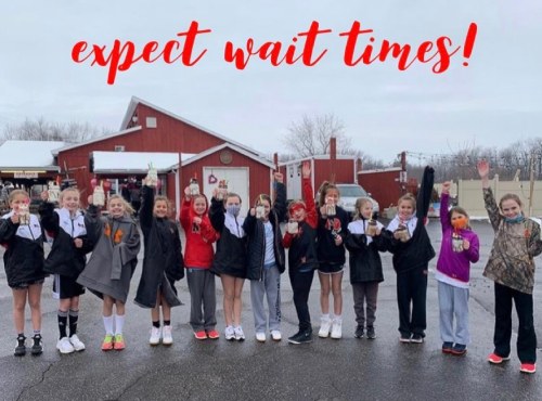 A group of young athletes stands outside, smiling and waving, with a red barn in the background and "expect wait times!" text.