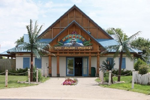 A tropical-themed building with palm trees, featuring a sign for "Kona Ice Golf Arcade Speedway."