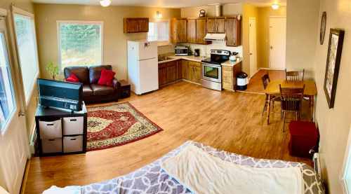 Cozy open-plan living space with a kitchen, dining area, and seating, featuring wooden floors and natural light.