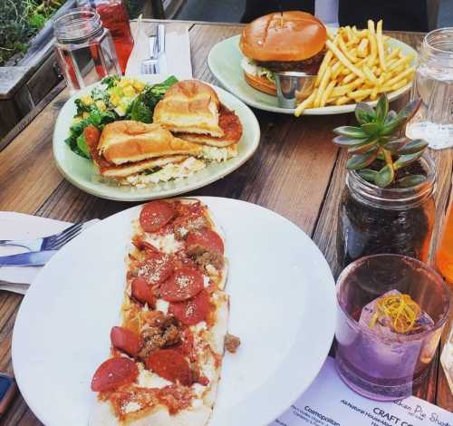 A table with a plate of pizza, a burger with fries, and a salad, all set in a casual dining environment.