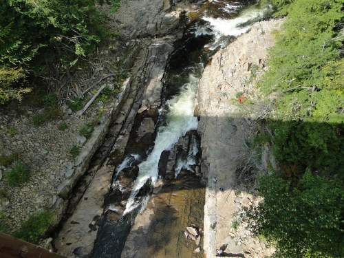 Aerial view of a rocky river with flowing water, surrounded by trees and rugged terrain.
