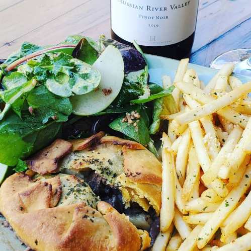 A plate with a salad, golden fries, and a pastry filled with greens, alongside a bottle of Russian River Valley Pinot Noir.