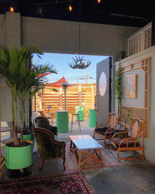 Cozy indoor seating area with plants, a rug, and a view of an outdoor patio with colorful furniture and string lights.