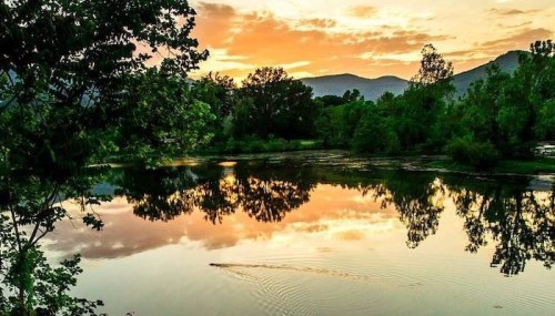 A serene lake at sunset, reflecting trees and mountains under a colorful sky.