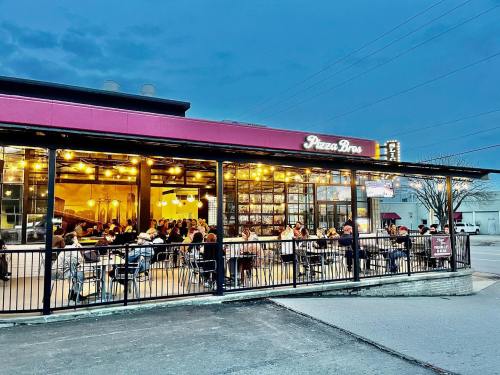 A bustling pizza restaurant with outdoor seating, filled with diners, under a twilight sky.