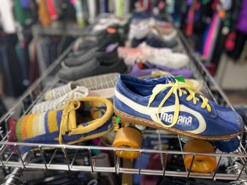 A rack of various shoes, including a blue sneaker with yellow laces and a yellow and blue striped slipper.