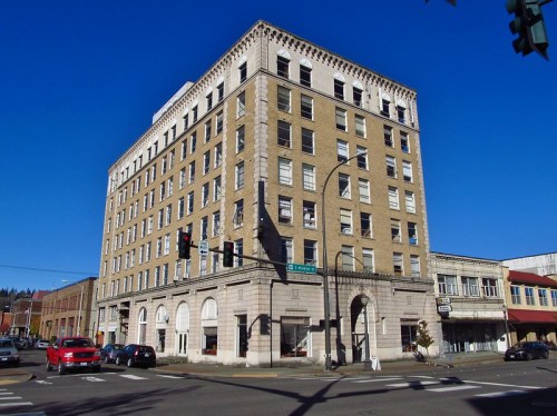 Historic brick building with multiple stories, featuring large windows and decorative cornice, set against a clear blue sky.