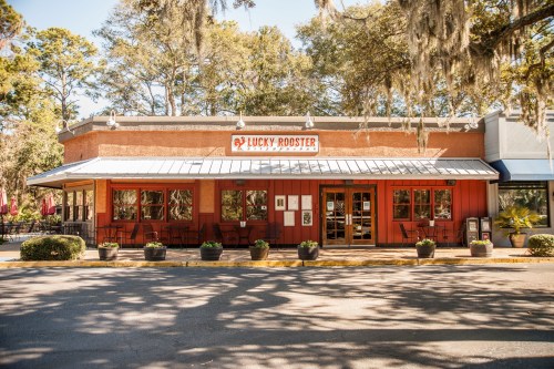Exterior view of Lucky Rooster restaurant, featuring a red facade, large windows, and surrounding greenery.