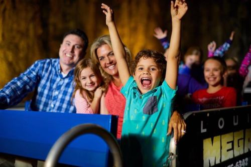 A joyful family on a roller coaster, with kids smiling and raising their hands in excitement.