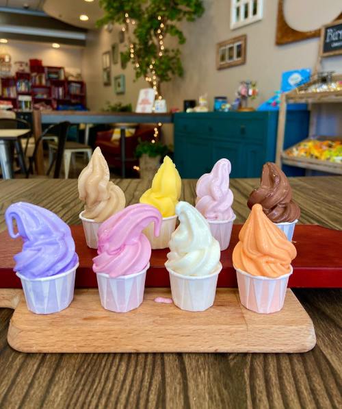 A colorful display of miniature ice cream cones in various flavors on a wooden board, set in a cozy café.