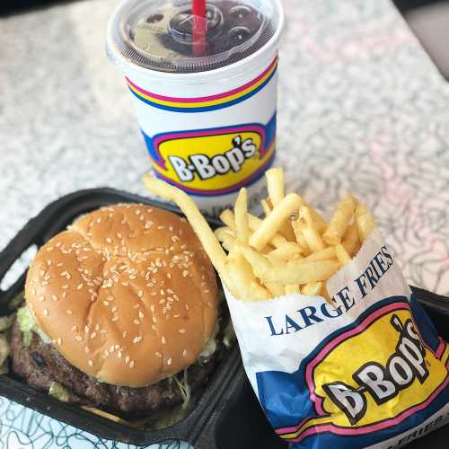 A burger with lettuce, a large fries container, and a drink from B-Bop's on a patterned table.