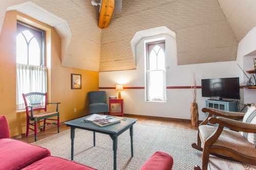 Cozy room with sloped ceilings, a red sofa, a blue chair, a coffee table, and a TV, featuring warm lighting and decor.