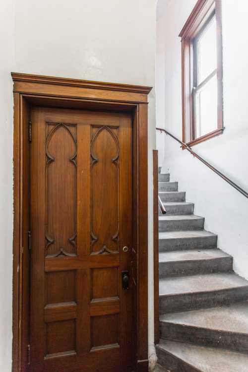 A wooden door with decorative carvings next to a staircase leading up, with a window at the top.