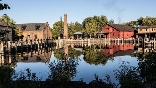 A serene waterfront scene with historic buildings reflecting in calm water under a clear blue sky.