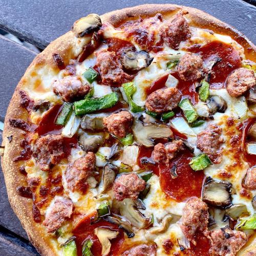 A close-up of a pizza topped with sausage, mushrooms, green peppers, and a rich tomato sauce on a golden crust.