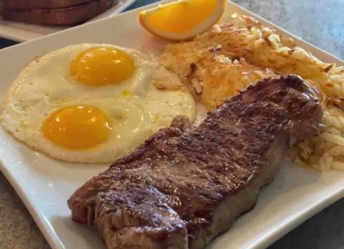 A plate featuring two sunny-side-up eggs, hash browns, a steak, and a slice of orange.