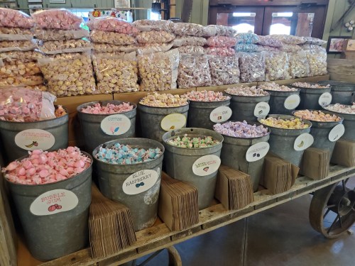 A display of colorful candy in buckets, with bags of assorted treats stacked in the background.