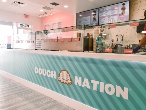 Interior of a dessert shop named "Dough Nation," featuring a colorful counter and menu displays.