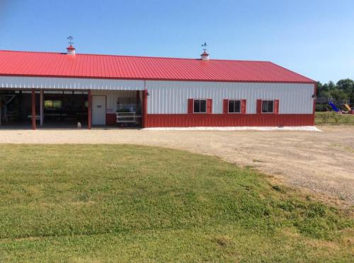 A red and white barn with a metal roof, set on a grassy area under a clear blue sky.