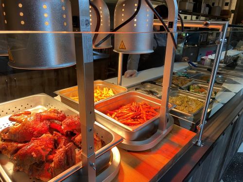 A food display with trays of roasted chicken, fries, and various side dishes under warming lamps in a restaurant setting.