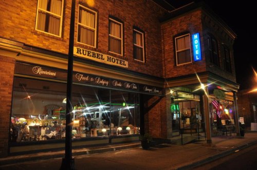 The Ruebel Hotel at night, featuring illuminated signs and a cozy storefront with various items on display.