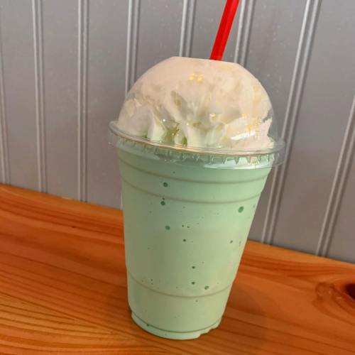 A mint green milkshake topped with whipped cream and a red straw, placed on a wooden table.