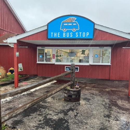 A red building with a blue sign reading "The Bus Stop," featuring a wooden ramp and flower pot in front.
