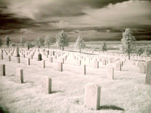A serene cemetery with rows of gravestones under a dramatic sky, captured in infrared.