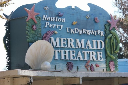 Sign for "Newton Perry Underwater Mermaid Theatre" adorned with marine-themed decorations like shells and sea creatures.