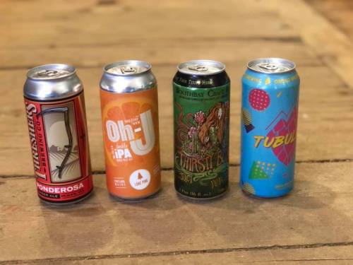 Four colorful beer cans lined up on a wooden surface, featuring distinct designs and labels.