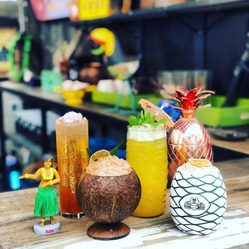 A colorful display of tropical cocktails and a hula dancer figurine on a bar counter.