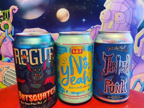 Three colorful beer cans: Rogue's "Batsquatch," Betts' "Y No Yeah," and Witch's Hat's "Trash Punk," against a vibrant backdrop.