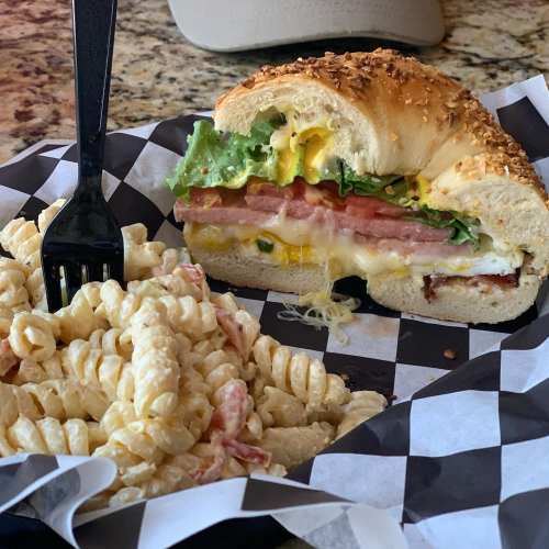 A sandwich with lettuce, tomato, and egg beside a serving of pasta salad on a checkered paper plate.
