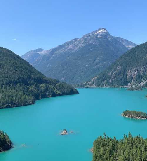 A stunning turquoise lake surrounded by lush green mountains and a clear blue sky.