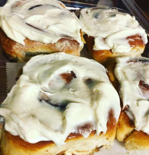 Four frosted cinnamon rolls arranged in a tray, showcasing their soft, swirled pastry and creamy icing.