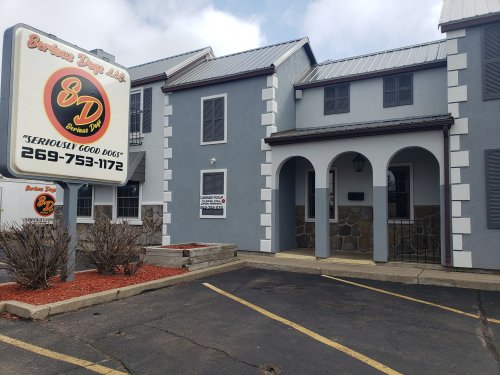 Exterior of a dog daycare building with a sign reading "Seriously Good Dogs" and a parking lot in front.