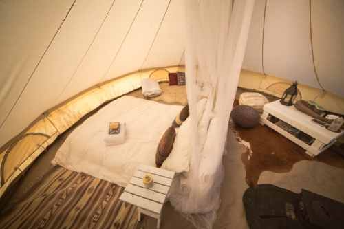 Cozy interior of a tent with a bed, cushions, a small table, and soft lighting, creating a warm atmosphere.