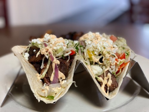 Two tacos filled with beef, lettuce, tomatoes, and cheese, topped with a creamy sauce, served on a plate.