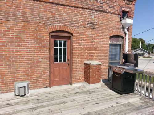 A brick wall with a wooden door, a window, and a grill on a wooden deck.