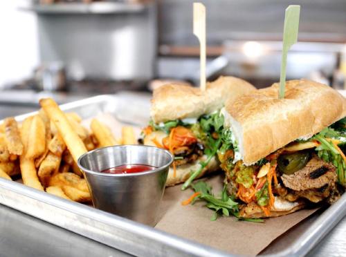 A tray with two large sandwiches topped with vegetables and two skewers, accompanied by crispy fries and a small cup of ketchup.