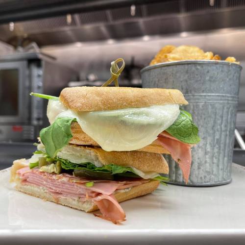 A layered sandwich with ham, lettuce, and cheese, served with a small bucket of chips on the side.