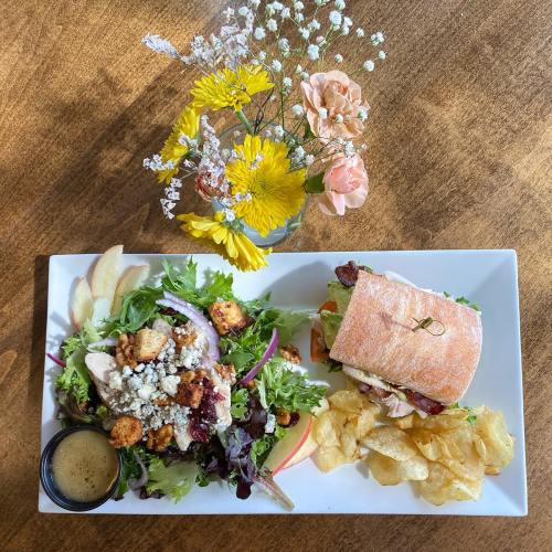 A plate with a salad, sandwich, and chips, accompanied by a small vase of flowers on a wooden table.
