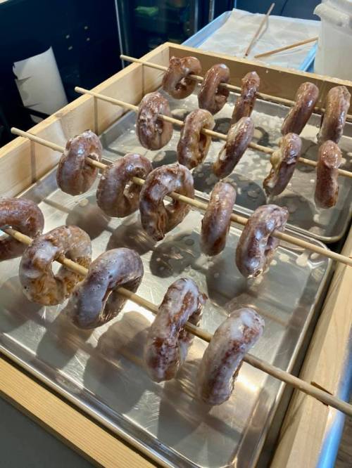 A tray of glazed donuts on skewers, arranged neatly in a wooden container.