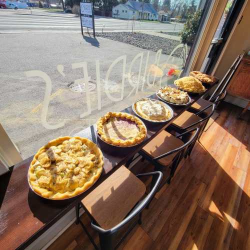 A display of various pies on a windowsill, with chairs lined up in front and a view of the street outside.