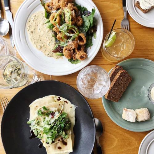 A table set with various dishes: a salad, fried food, a creamy pasta, and drinks, all on wooden surfaces.