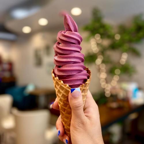 A hand holds a cone with swirled purple soft serve ice cream against a blurred background.