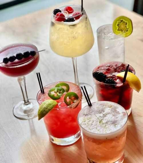 A variety of colorful cocktails with fruits and garnishes on a wooden table.