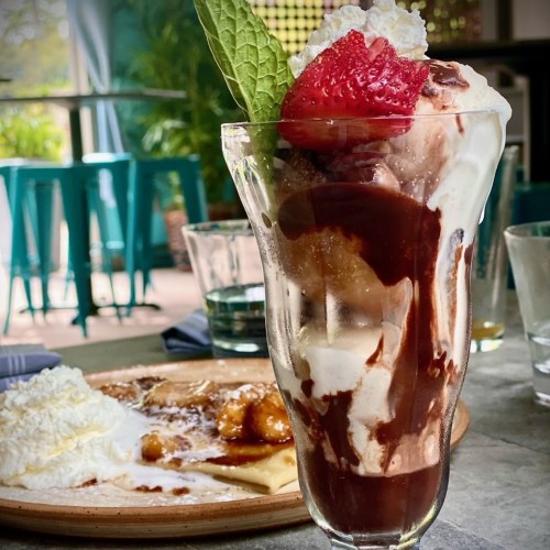 A delicious sundae with chocolate sauce, whipped cream, a strawberry, and a mint leaf, alongside a plate of dessert.