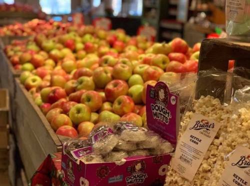 A market display filled with various apples, alongside bags of popcorn and snacks on a wooden table.